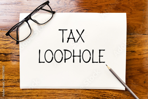 Tax loophole text on blank notebook paper on wooden table with pencil and glasses aside. Business concept and legal concept about tax loophole. photo