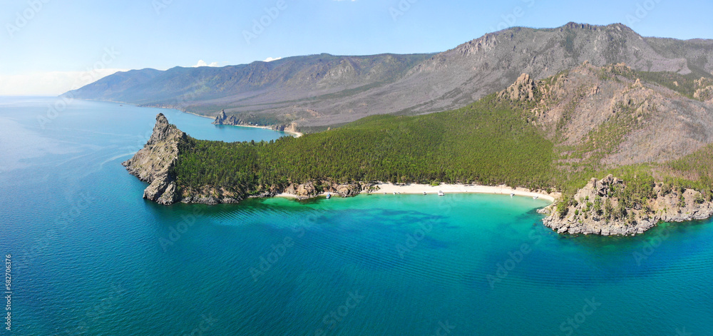 Panorama of the bay with a sandy beach and turquoise water color. Picturesque summer landscape. Mountains with coniferous forest. Aerial view