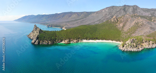 Panorama of the bay with a sandy beach and turquoise water color. Picturesque summer landscape. Mountains with coniferous forest. Aerial view