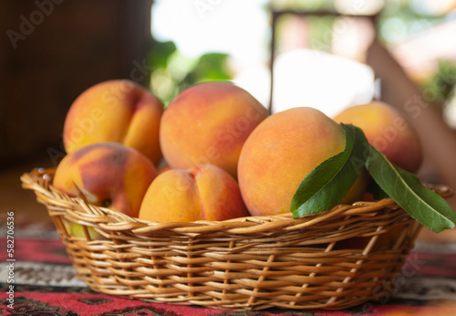 Fresh peaches fruits with leaves in basket on rustic background