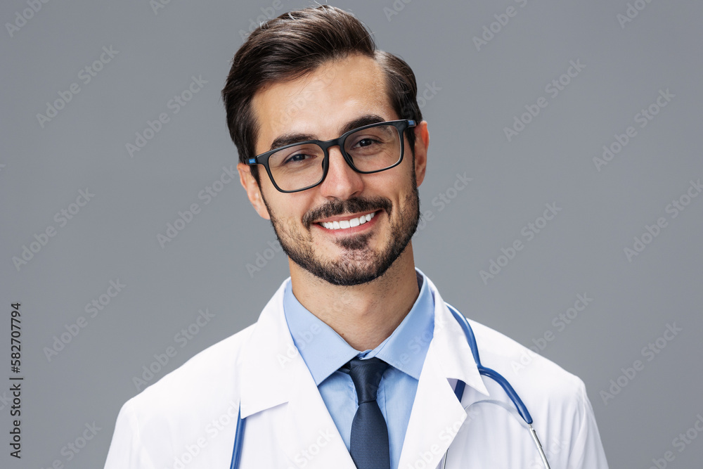 Male doctor in a white coat and glasses for vision and a stethoscope looks at the camera smile with teeth dentist on a gray isolated background, copy space, space for text, health Male doctor in a white coat and glasses for vision and a stethoscope looks at the camera smile with teeth dentist on a gray isolated background, copy space, space for text, health