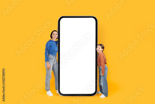 Happy Mother And Daughter Standing Near Big Blank Smartphone With White Screen