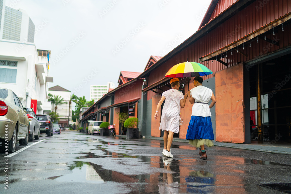 Asian drag queen gay friends in woman clothes holding umbrella walking down city street together in raining day. Diversity sexual equality, lgbtq pride people and transgender cross-dressing concept. Asian drag queen gay friends in woman clothes holding umbrella walking down city street together in raining day. Diversity sexual equality, lgbtq pride people and transgender cross-dressing concept.