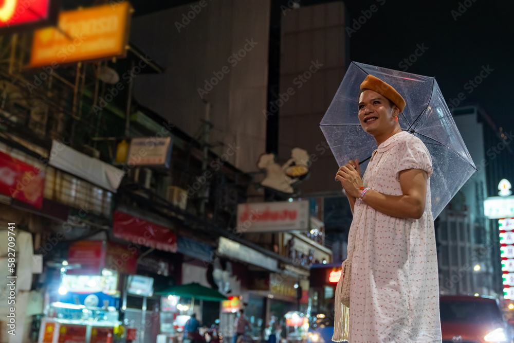 Happy Asian guy drag queen in woman clothes and makeup holding umbrella walking down city street in raining night. Diversity sexual equality, lgbtq pride people and transgender cross-dressing concept.
