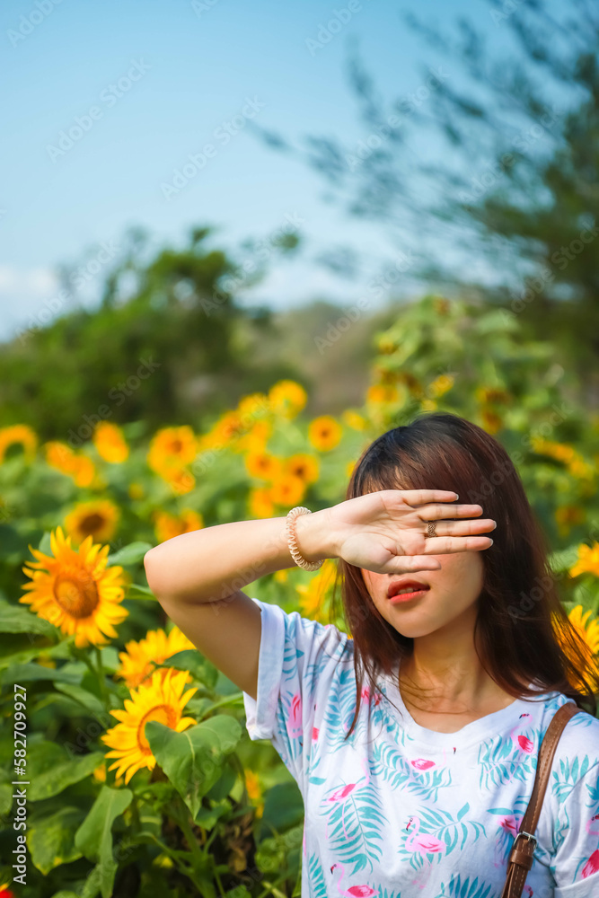 A beautiful asian girl was covering her face with her hands because the sun was so bright during the day with flower field background. Concept for skin care, beauty and ultraviolet sunscreen. A beautiful asian girl was covering her face with her hands because the sun was so bright during the day with flower field background. Concept for skin care, beauty and ultraviolet sunscreen.