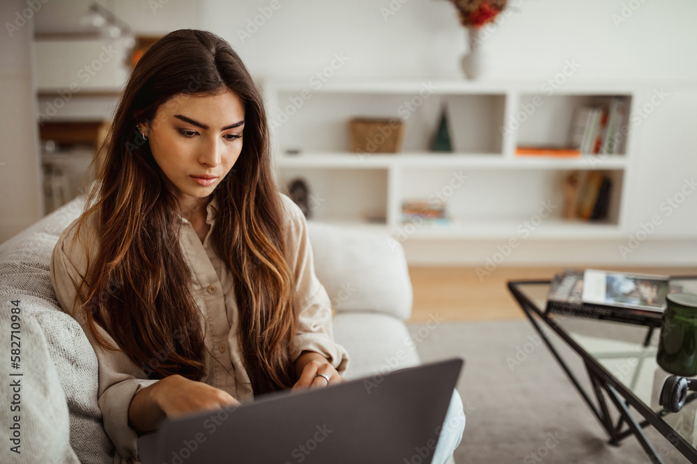 Busy serious millennial mixed race lady typing on laptop in living room interior, close up Busy serious millennial mixed race lady typing on laptop in living room interior, close up