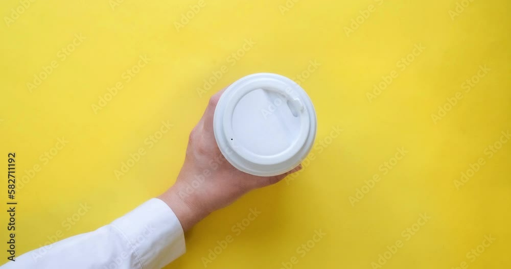 Craft paper coffee cup fills with drink and woman's hand take it. Coffee to go in a cup with a white lid on a yellow background. Looped 4K stop motion animation