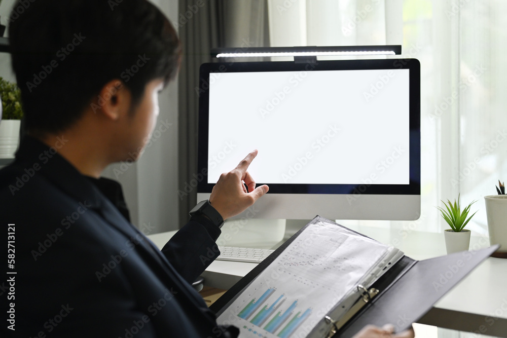 Back view of young man investor looking at computer monitor, analyzing project statistics or statistics data at workplace Back view of young man investor looking at computer monitor, analyzing project statistics or statistics data at workplace