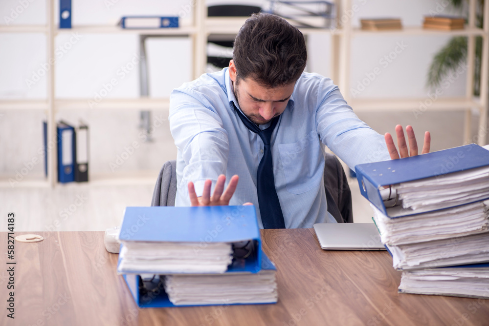 Young male employee and too much work in the office Young male employee and too much work in the office