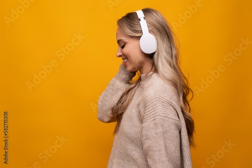 cute lady joyfully listens to music with big headphones on orange background
