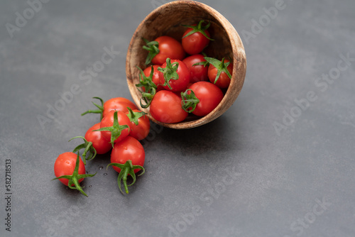Cherry tomatoes pouring from a wooden bowl on a black background