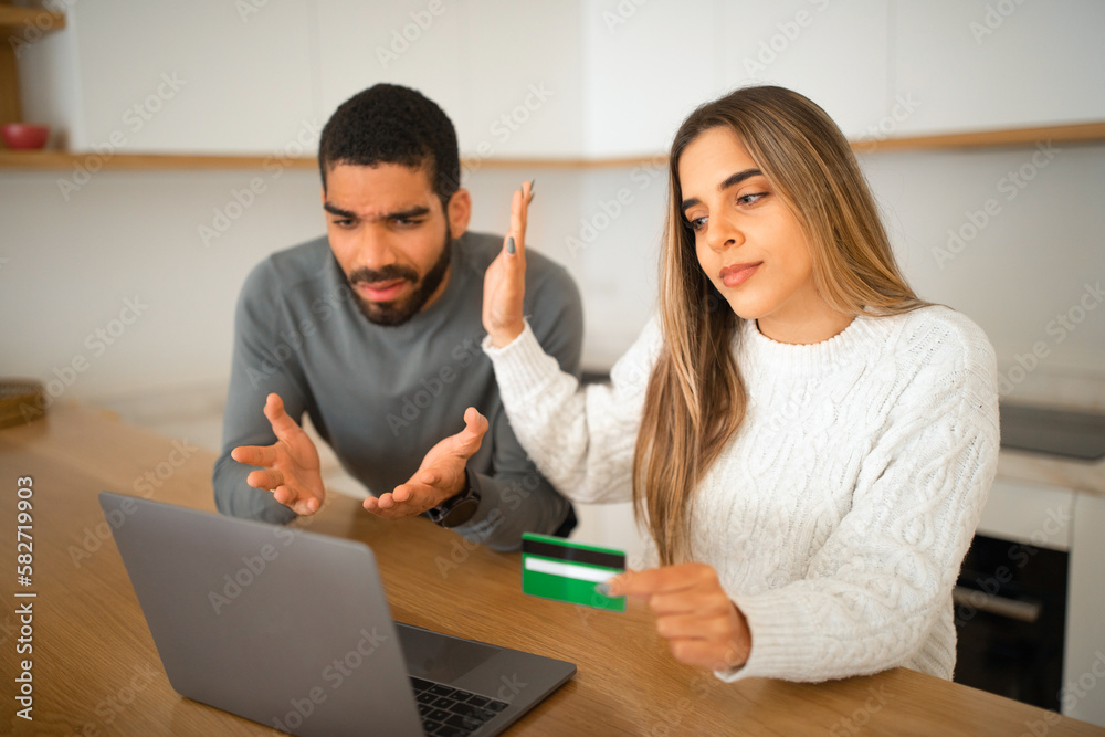 Sad offended international millennial couple pointing hands at laptop, use credit card, online shopping Sad offended international millennial couple pointing hands at laptop, use credit card, online shopping