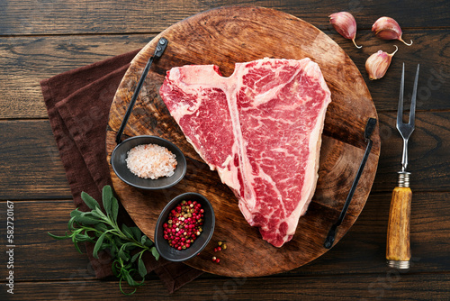 Thick Raw T-Bone Steak. Dry-aged Raw T-bone or porterhouse beef meat Steak on cutting boar with herbs and salt on dark background. Top view and copy space.