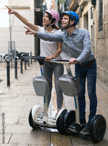 young couple guy and girl walking on segway in streets of european city