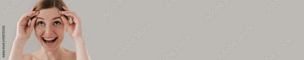 What is that? Portrait of attractive woman with freckles on face touching her eyebrows and smiling while standing against background What is that? Portrait of attractive woman with freckles on face touching her eyebrows and smiling while standing against background