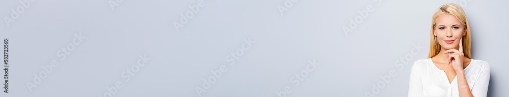 Attractive young blond hair woman holding hand on chin against grey background Attractive young blond hair woman holding hand on chin against grey background
