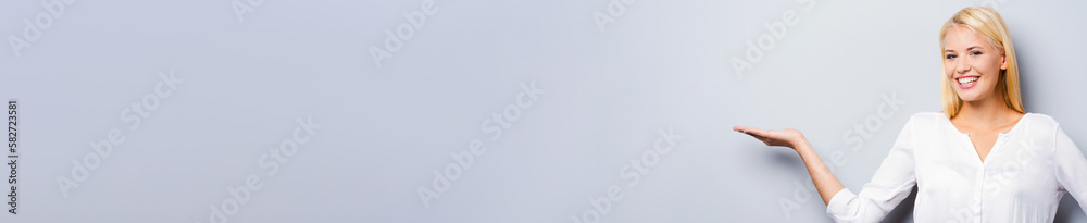 Happy young women pointing copy space while standing against grey background Happy young women pointing copy space while standing against grey background