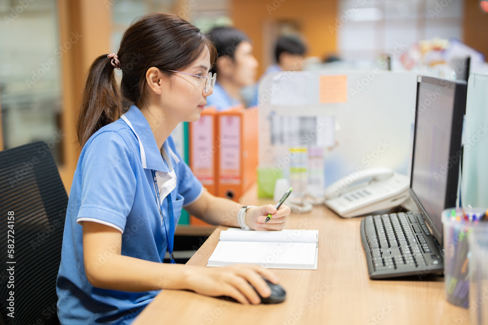 Caucasian female worker wearing eyeglasses in a company office talking on the phone in front of the computer Dressed in uniform, on the desk, there are papers, pens, and a phone. Caucasian female worker wearing eyeglasses in a company office talking on the phone in front of the computer Dressed in uniform, on the desk, there are papers, pens, and a phone.
