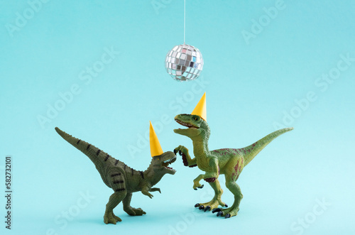 Two cute green dinosaurs dancing under disco ball. Funny idea for birthday card on blue background. © dvulikaia