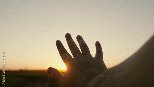Mans hand reaches for sun, rays of sun break through his fingers. Hand of happy person reaches for sun. Sunset between fingers. Dream travelers hand, sun. Adventure, travel. Mans prayer in nature