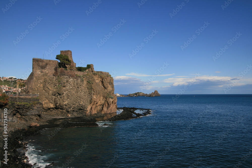 The Fortress of Aci Castello dominates the Mediterranean sea from volcanic rocks in a sunny day. Cyclopes Bay, Sicily, Italy
