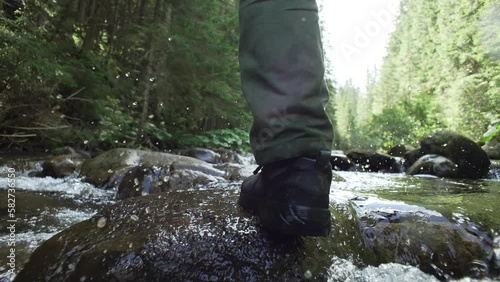 A man walks across a mountain river, leg close-up, summer, green forest. Tourist on a hike, outdoors. River crossing. Get your feet wet. High quality 4k footage