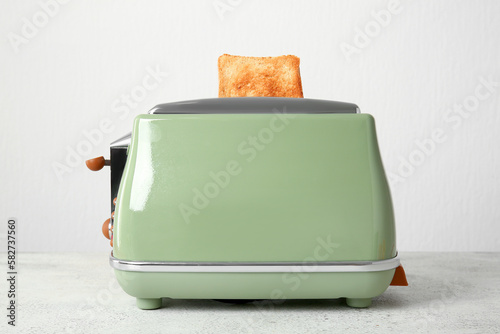 Modern toaster with crispy bread slice on white table