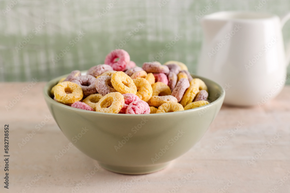 Bowl of colorful cereal rings and pitcher with milk on white wooden table near green wall Bowl of colorful cereal rings and pitcher with milk on white wooden table near green wall