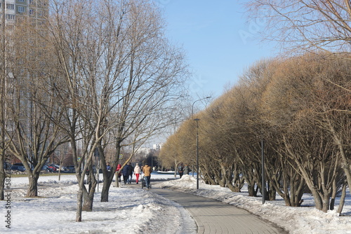 Alley in the park with melting snow, puddles and ice in spring. Butovo, Moscow, thawed patches, March 2023.