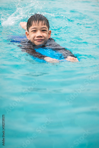 Cute Little Asian Thai Boy, practicing swimming in the pool.