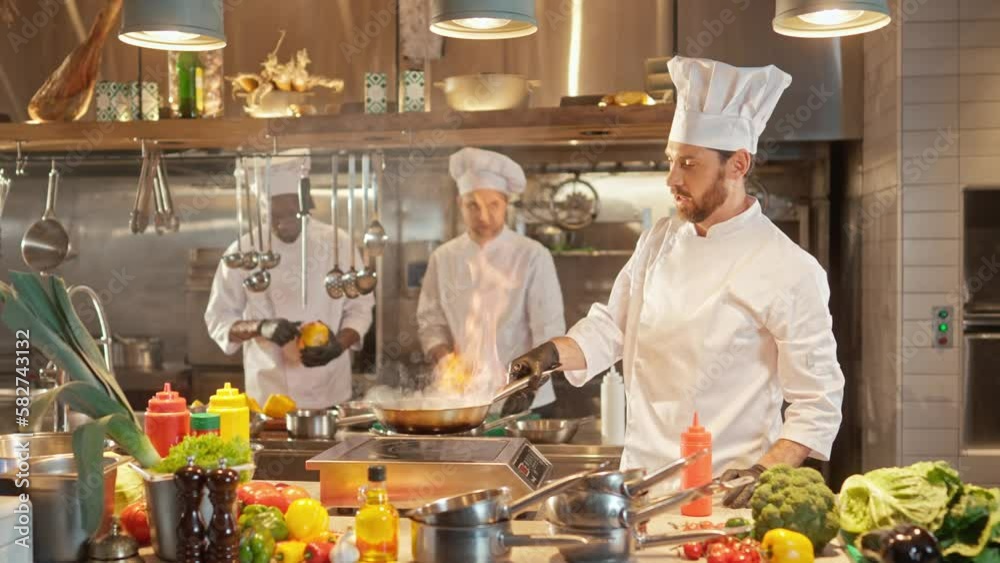 Portrait of beautiful professional caucasian chef cooking vegetables frying on pan and mixing. Attractive skillful bearded male cook working at modern hotel kitchen smiling enjoying work. Portrait of beautiful professional caucasian chef cooking vegetables frying on pan and mixing. Attractive skillful bearded male cook working at modern hotel kitchen smiling enjoying work.
