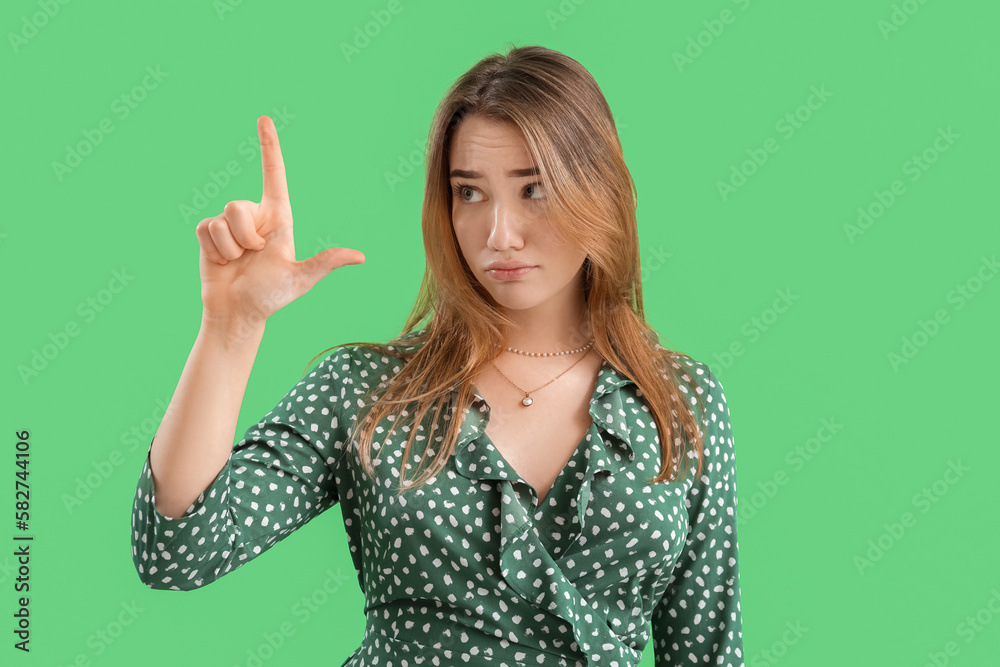 Upset young woman showing loser gesture on green background