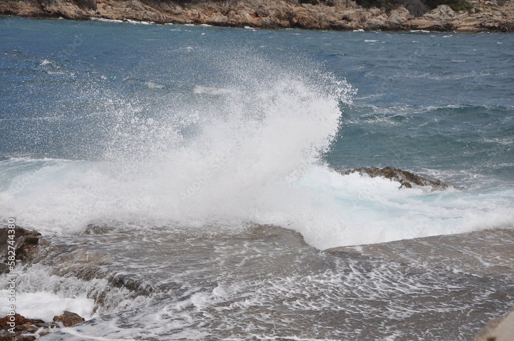 Fototapeta premium Wave breaking on the beach.Breaking sea wave on the rocky coast.The sea wave crashing on the rock and make the splashing water and white air foam bubble. Wave breaking on the beach.