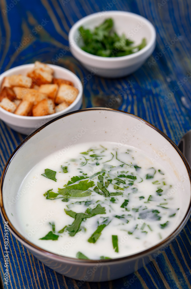yogurt soup with herbs and crackers on a blue wooden table yogurt soup with herbs and crackers on a blue wooden table