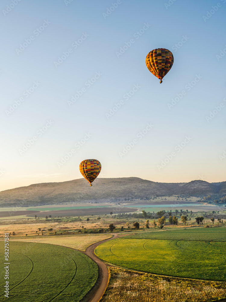Two colourful hot air balloons flying over circular crop field during sunrise in Magaliesburg, Gauteng, South Africa