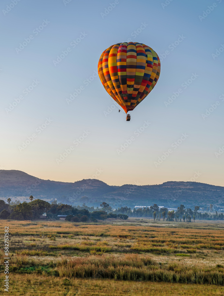 Obraz premium Colourful hot air balloon flying over a grass field during sunrise in Magaliesburg, Gauteng, South Africa