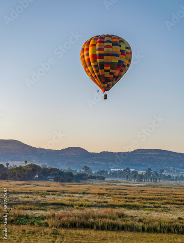Colourful hot air balloon flying over a grass field during sunrise in Magaliesburg, Gauteng, South Africa © Arnold