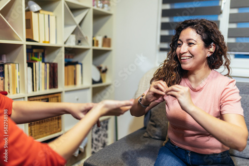 Deaf woman speaking sign language with her friend, sitting on couch. photo