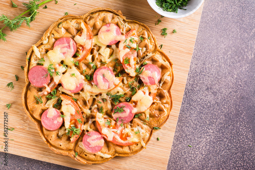 Slika na platnu Closeup of waffle pizza with tomatoes, sausages, cheese and herbs on a wooden board