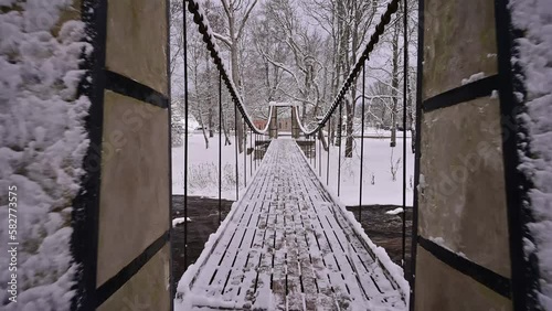 Crossing a winter river through a snowy suspension bridge with strong chains.
