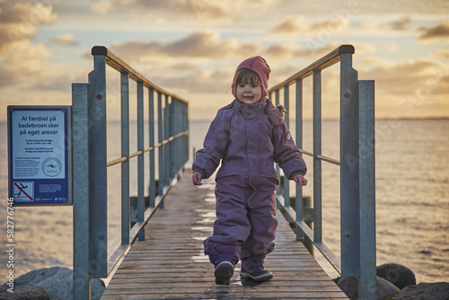 Fototapeta Naklejka Na Ścianę i Meble -  Adorable child walking on the pier in the evening in Denmark