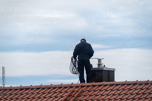Leinwand Poster Chimney sweeper on the roof of a house in an attempt of chimney sweeping