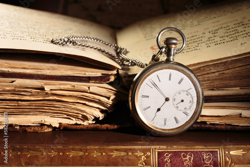 Antique pocket watch on opened antique books. Old bible on background