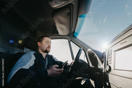 male truck driver with a smartphone in his hands is driving, shipping. © velimir