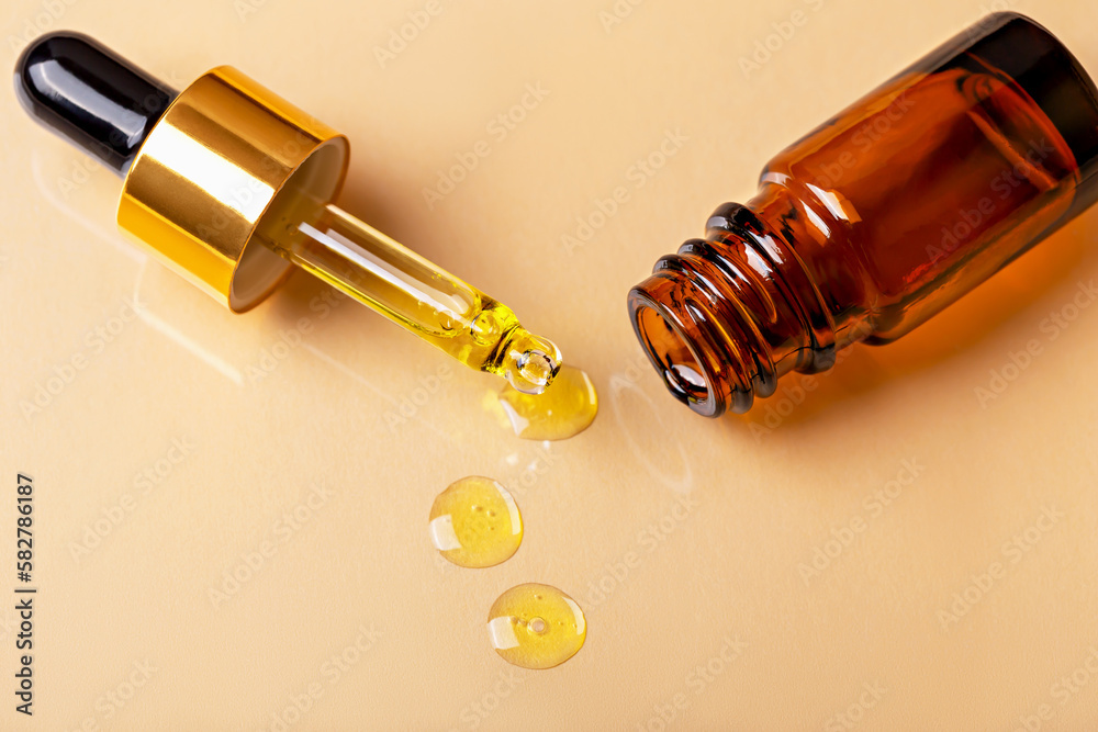 Laboratory studies. Dropper with drops of yellow liquid and glass amber cosmetic bottle on beige background close-up. Pipette with solution, essence, serum, emulsion. Natural organic cosmetics Laboratory studies. Dropper with drops of yellow liquid and glass amber cosmetic bottle on beige background close-up. Pipette with solution, essence, serum, emulsion. Natural organic cosmetics