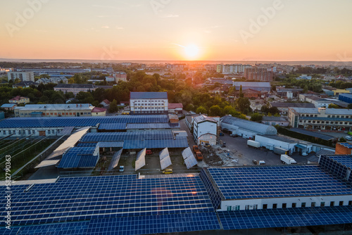 Aerial view of solar power plant with blue photovoltaic panels mounted on industrial building roof for producing green ecological electricity at sunset. Production of sustainable energy concept
