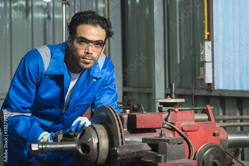 Caucasian Industry engineering wearing safety uniform, gloves and glasses control operating lathe grinding machine working in industry factory, looking at camera. Professional worker with skill