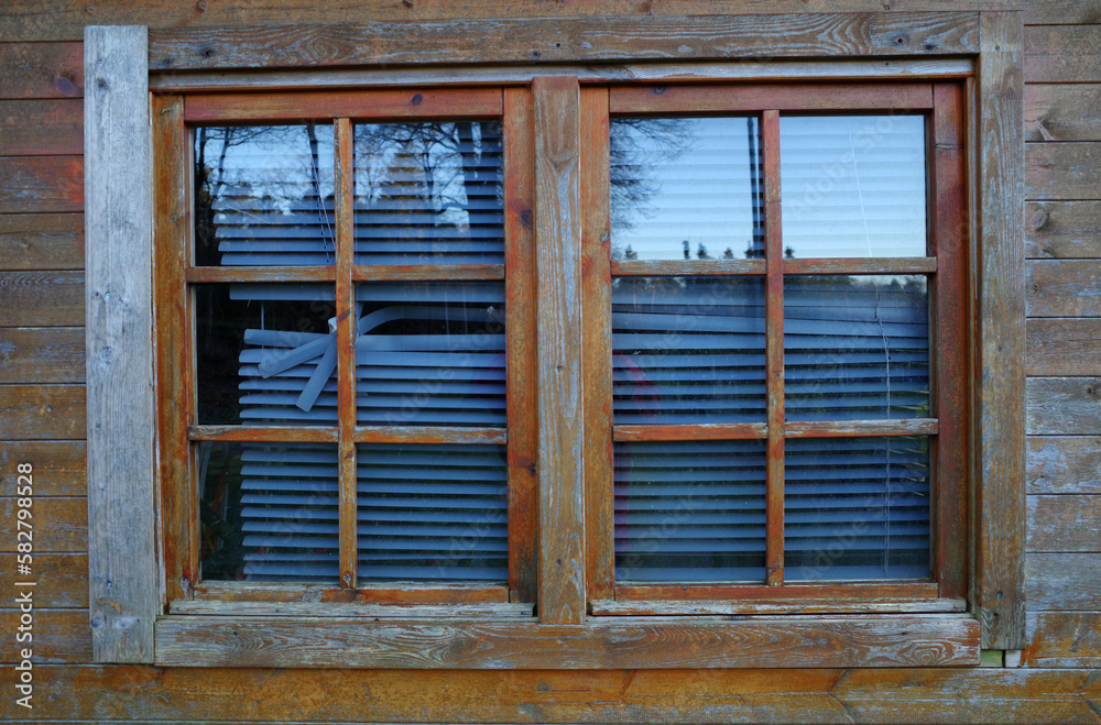 A window in a garden shed with broken blinds. The stained wood has also seen better days