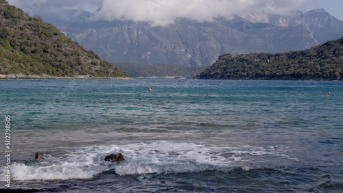 A Foamy small wave rolls onto the shore. The calm landscape of the sea in the middle of the mountains
