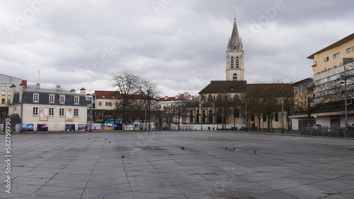 Grande place publique centrale d'une commune parisienne, mouillé et humide, temps pluvieux et nuageux, avec des habitations et une église, place de marchés locaux non occupés, personne et vide